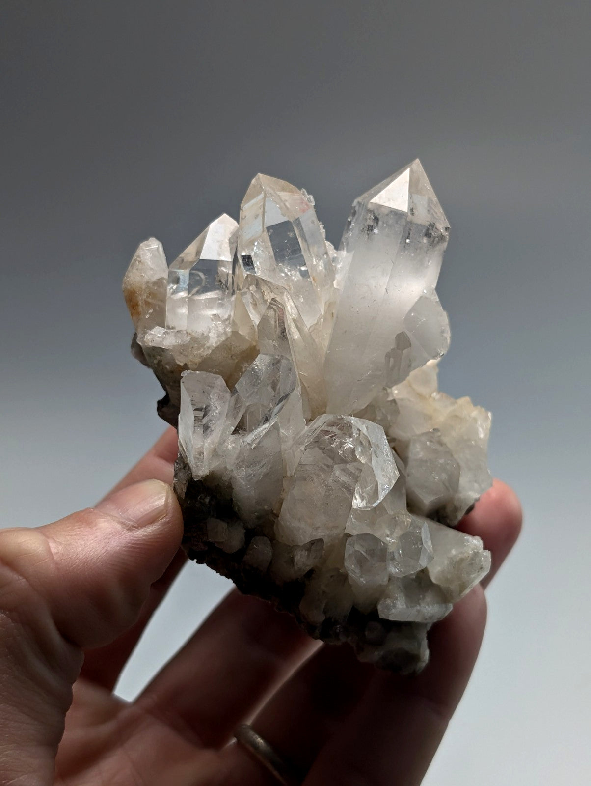 A translucent quartz crystal cluster with pointed, faceted formations and a base of dark mineral matrix.