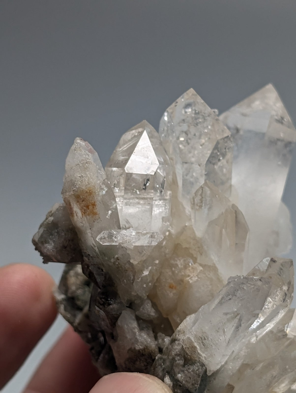 A cluster of clear, translucent quartz crystals with sharp, pointed facets and a few subtle brownish inclusions.