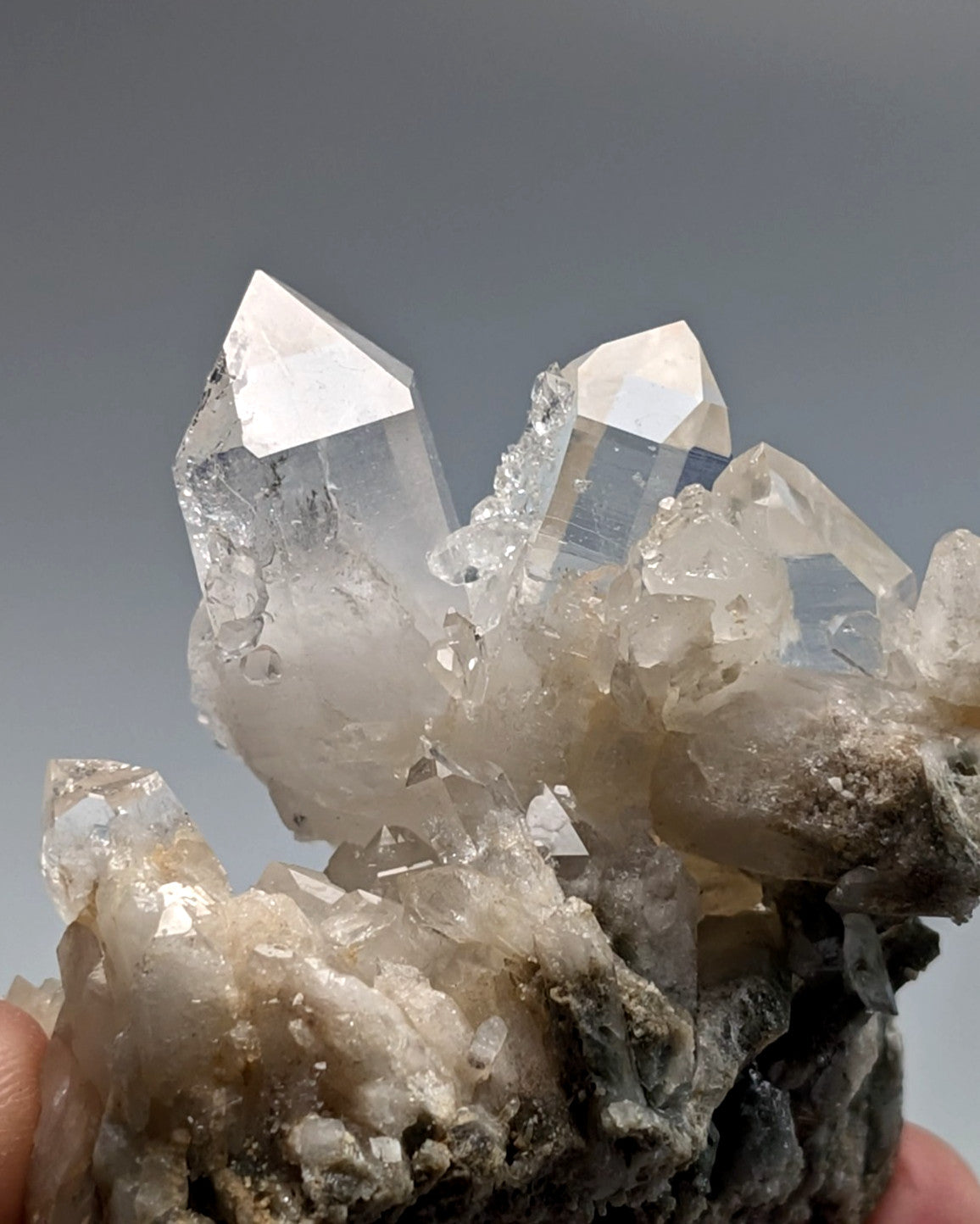 A cluster of clear, translucent quartz crystals with sharp, pointed tips and a rough, earthy base.