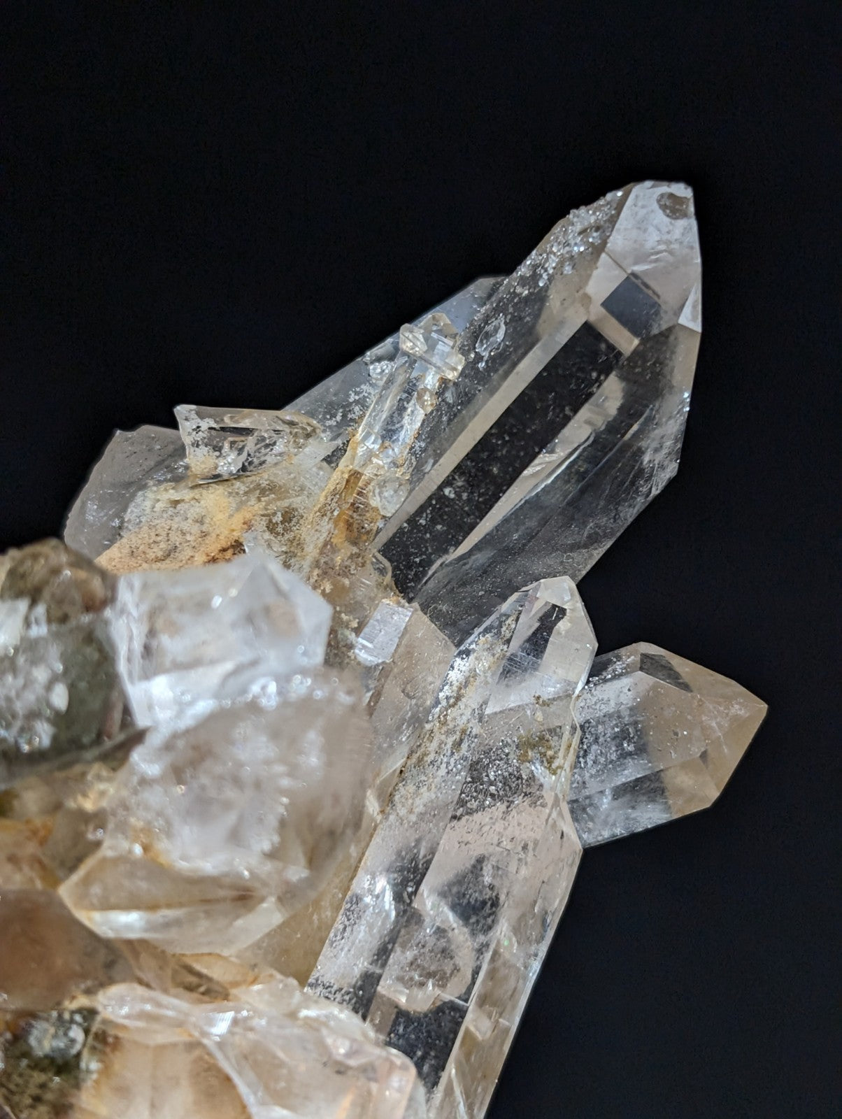 A cluster of clear, faceted quartz crystals with some exhibiting subtle golden hues and rougher, earthy bases.
