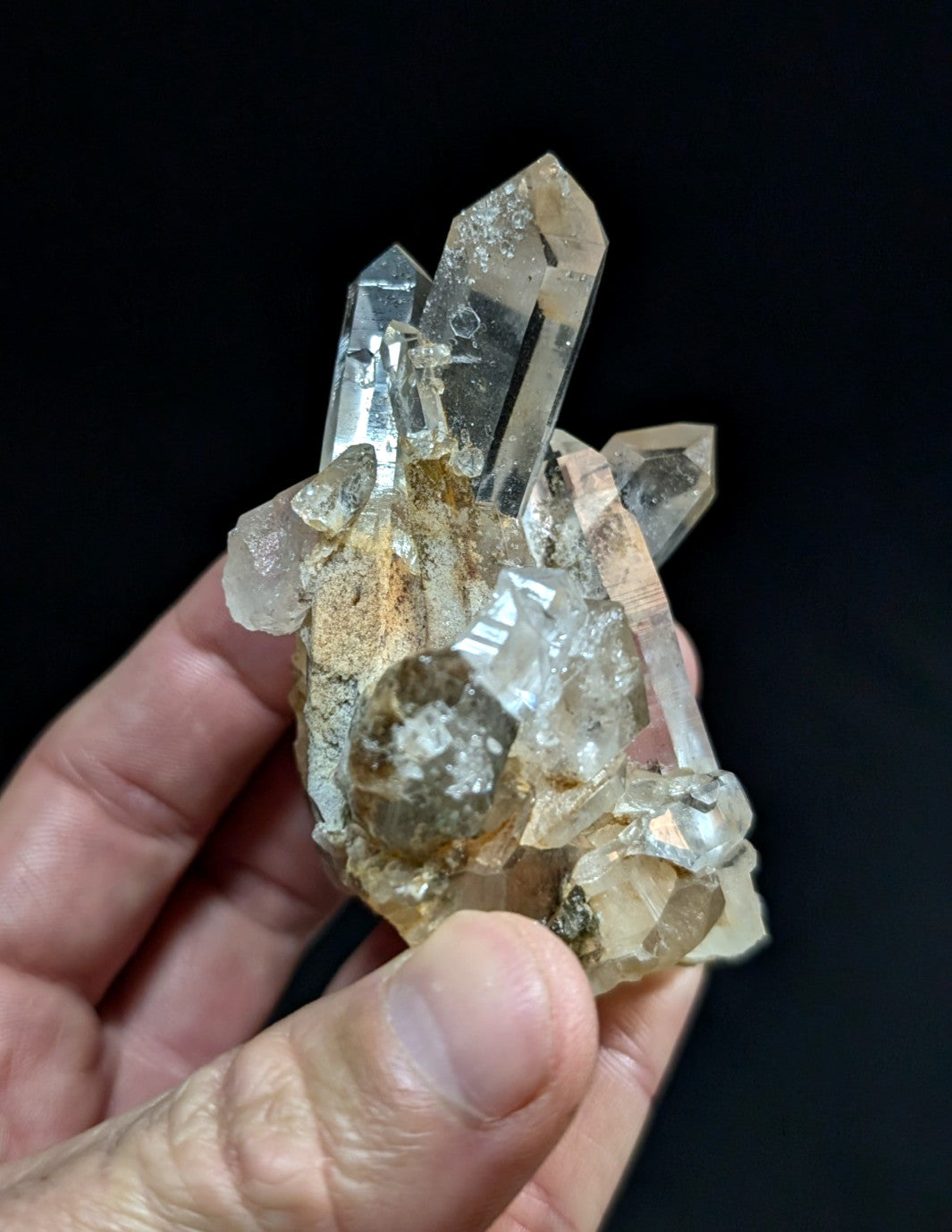 A clear quartz crystal cluster with transparent, faceted points and a base of earthy brown matrix.