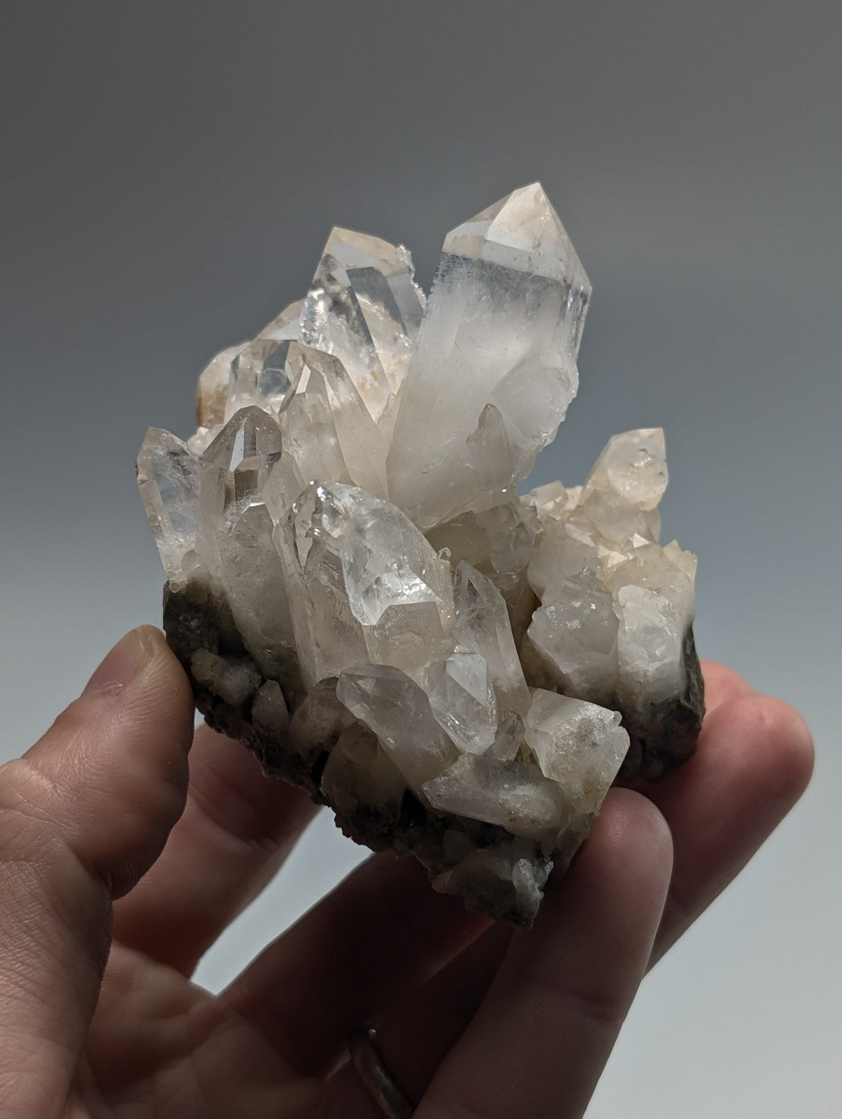 A translucent white quartz crystal cluster with sharp, pointed facets and a dark mineral base.