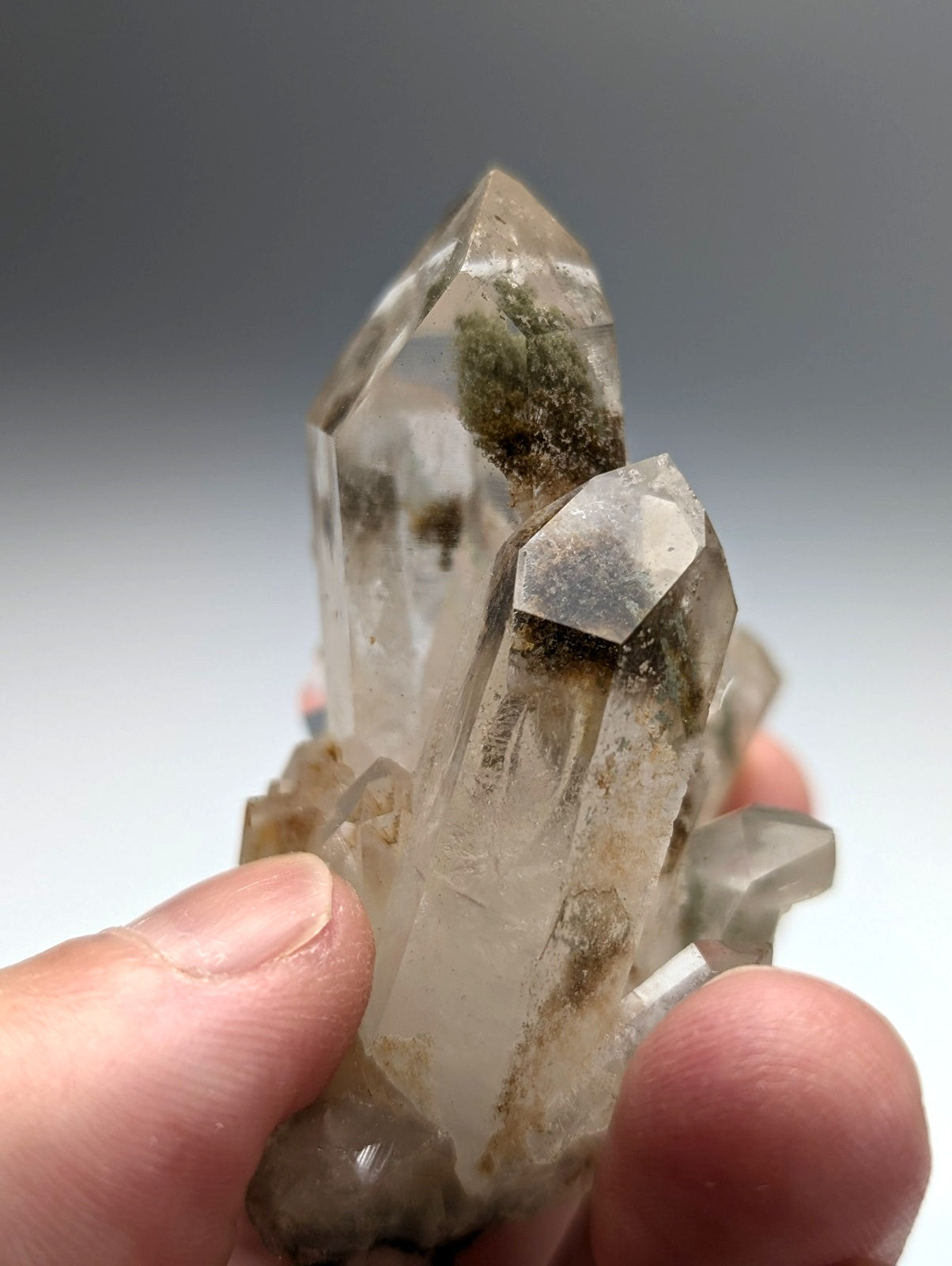 A cluster of clear chlorite phantom quartz crystals with green moss growth held in hand from willis mine arkansas