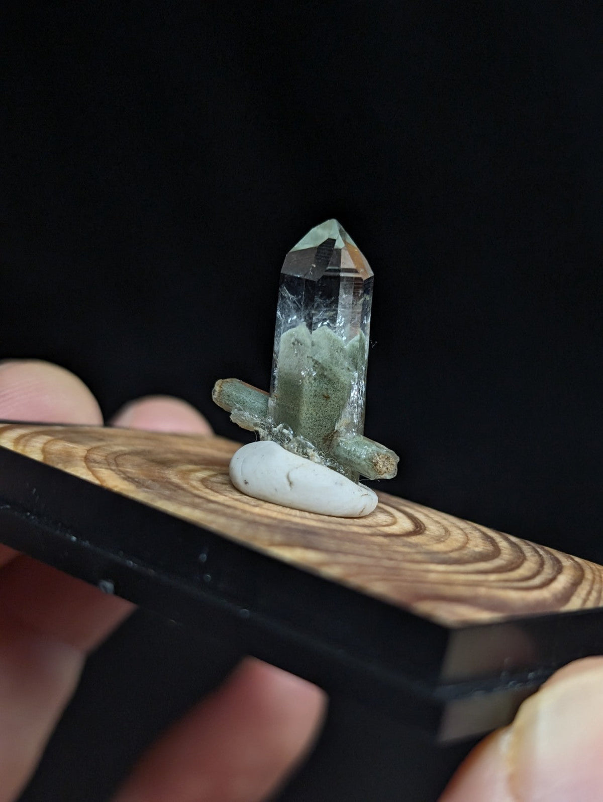 A translucent green quartz crystal with a pointed tip, mounted on a wooden display base.