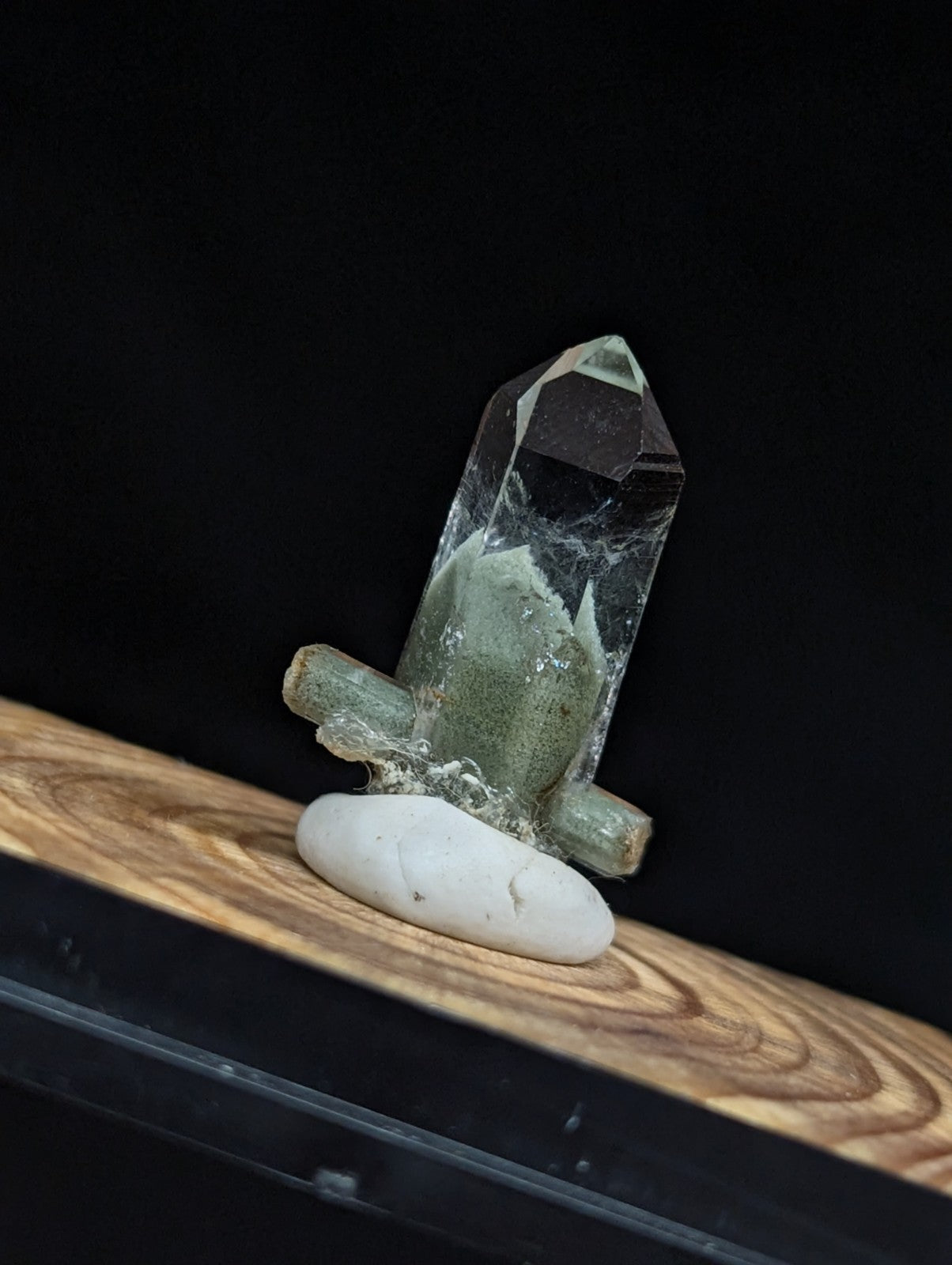 A translucent green crystal with a pointed tip and embedded white veining, mounted on a smooth white stone base.
