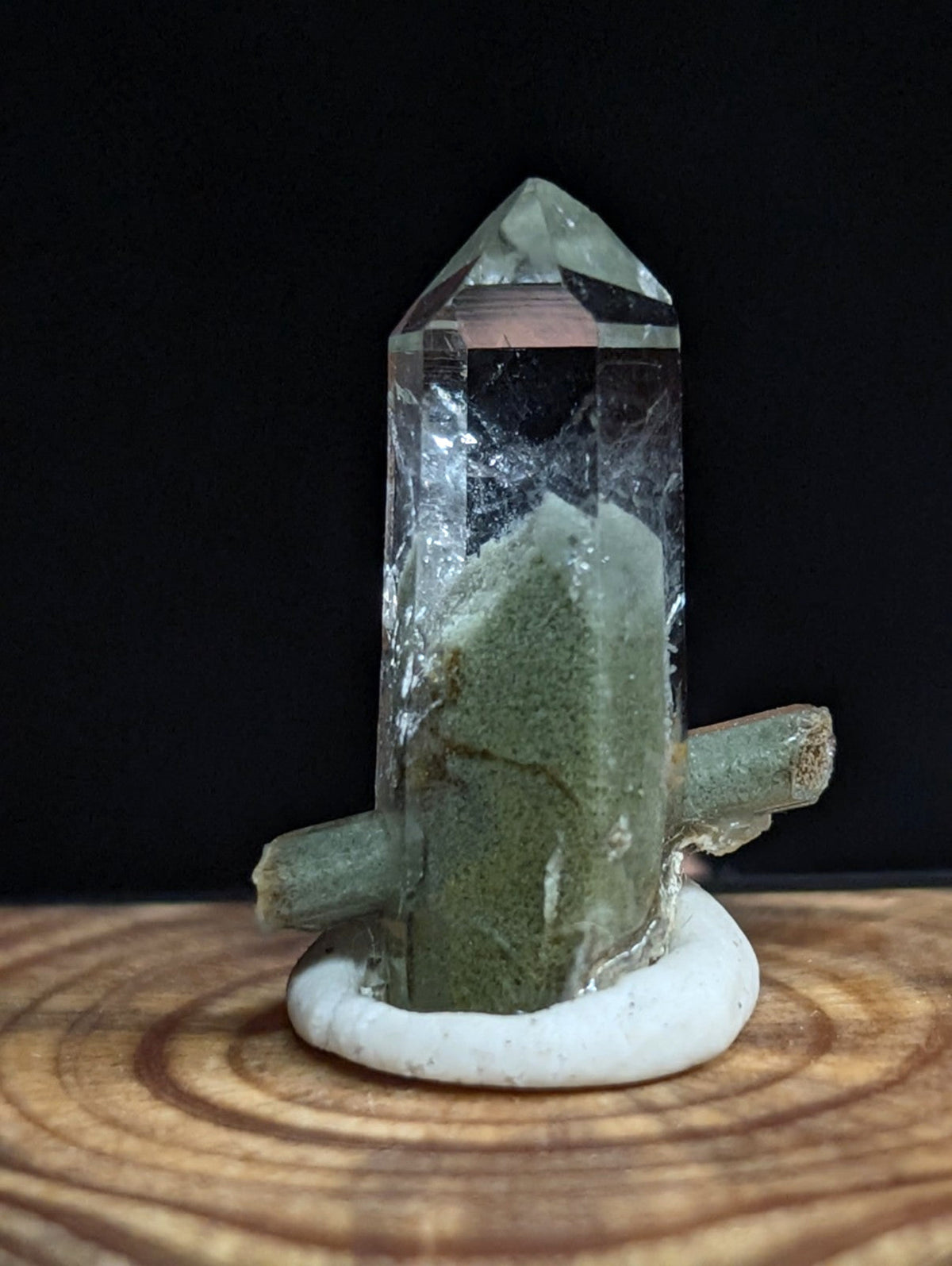 A clear quartz crystal with a greenish mineral inclusion, mounted on a white circular base.