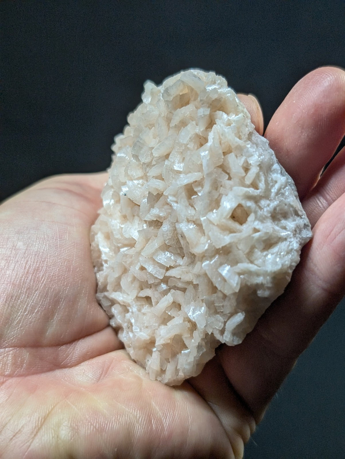 A translucent, pale white crystal cluster with a rough, jagged surface held in someone’s hand.