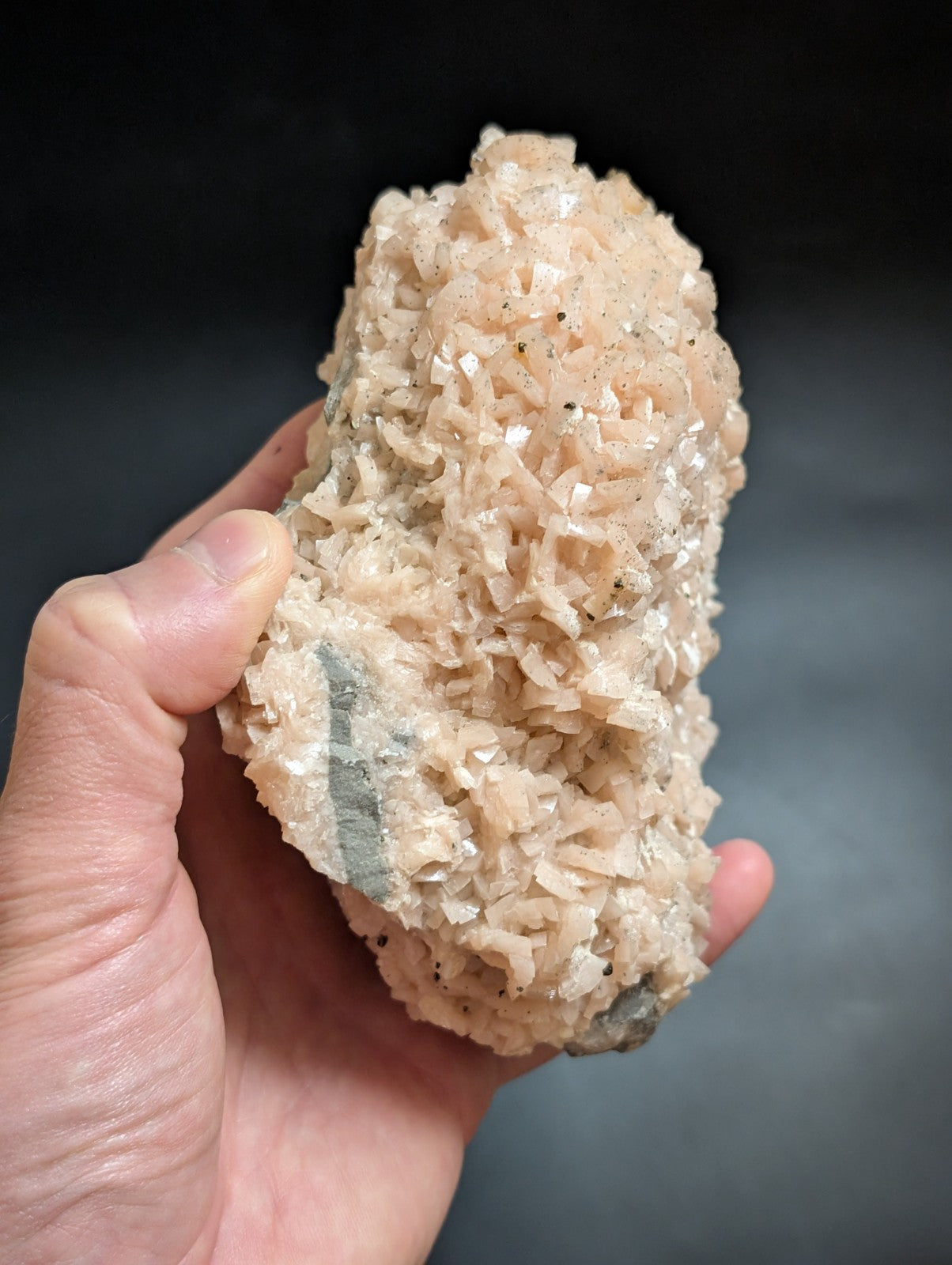 A hand holds a pale pink, crystalline mineral specimen with translucent facets and subtle gray veining.