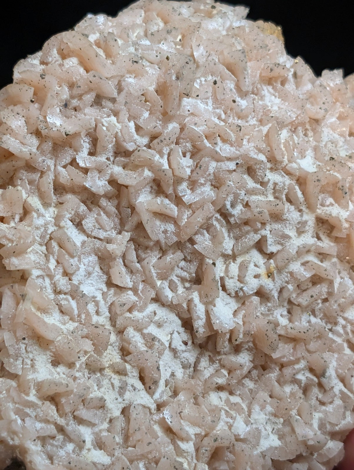 A pile of translucent, pale pinkish-white crystalline fragments with a powdery coating and speckled dark flecks.