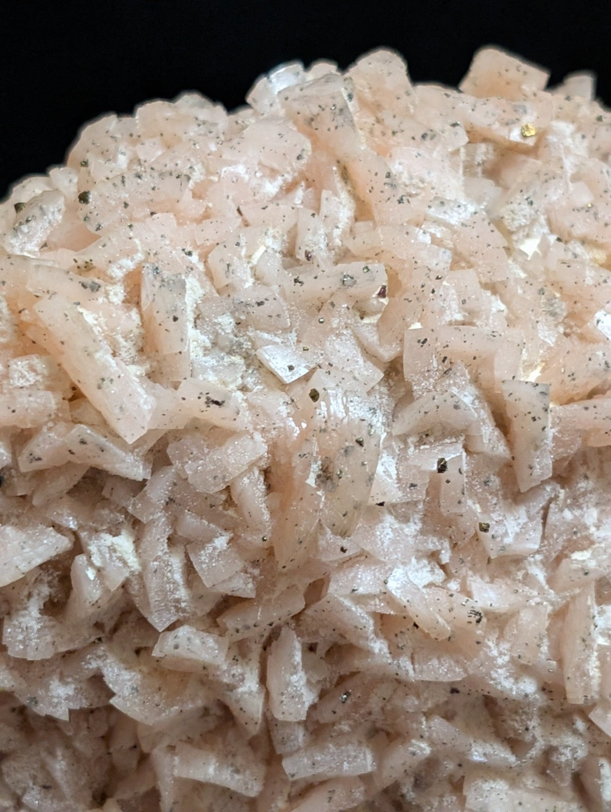 A cluster of translucent, pale pink crystalline minerals with embedded dark specks.