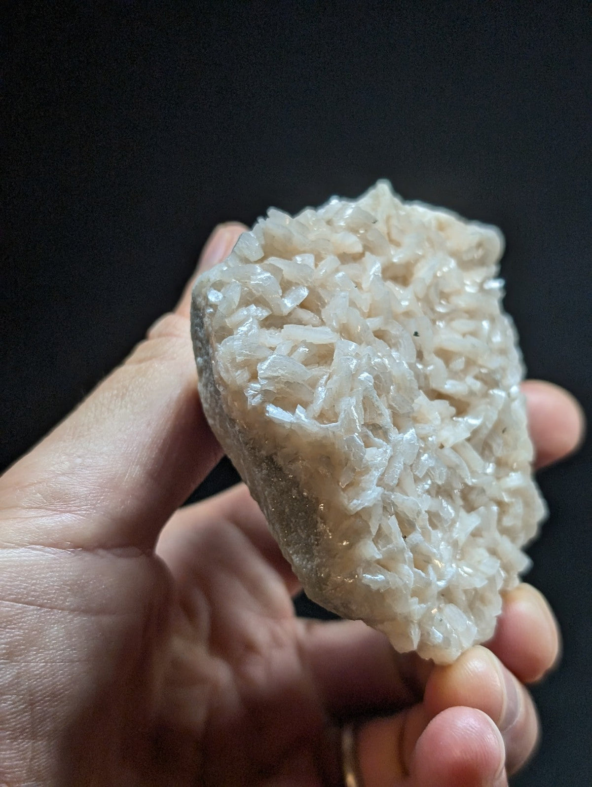 A hand holds a translucent, off-white quartz crystal cluster with intricate, jagged facets and a rough, natural base.