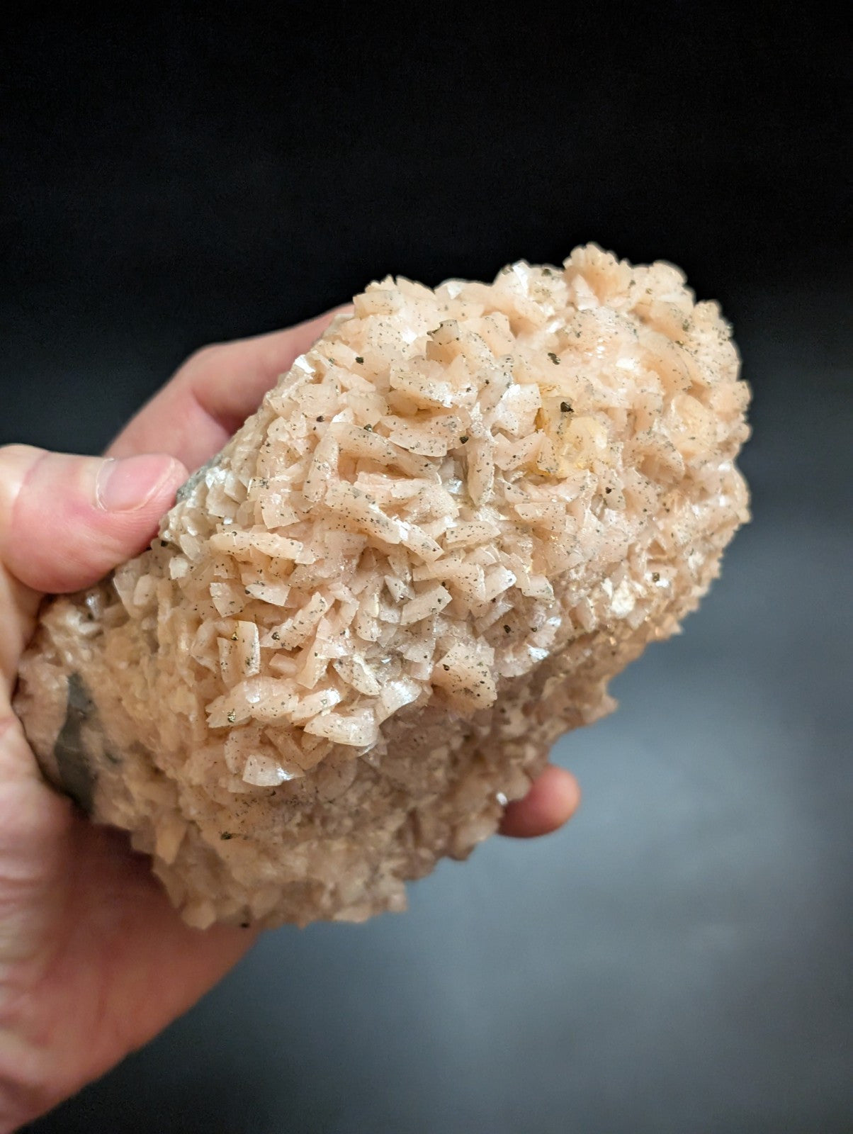 A hand holds a pale, translucent mineral specimen with intricate crystalline formations and subtle speckles.