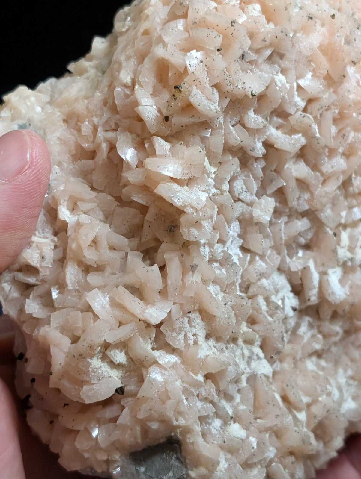 A cluster of translucent, pale pink crystalline minerals with a rough, jagged surface and scattered dark specks.