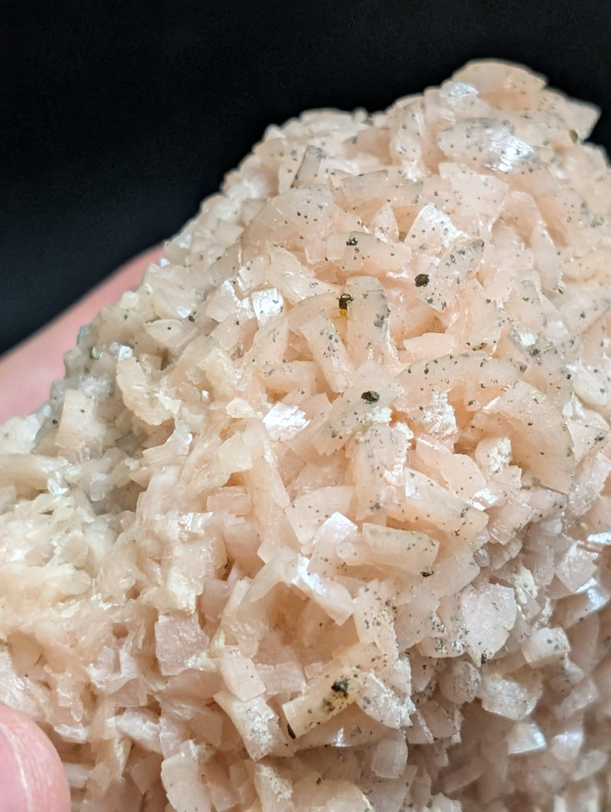 A cluster of translucent pinkish-white crystals with a rough, jagged surface and scattered dark specks.