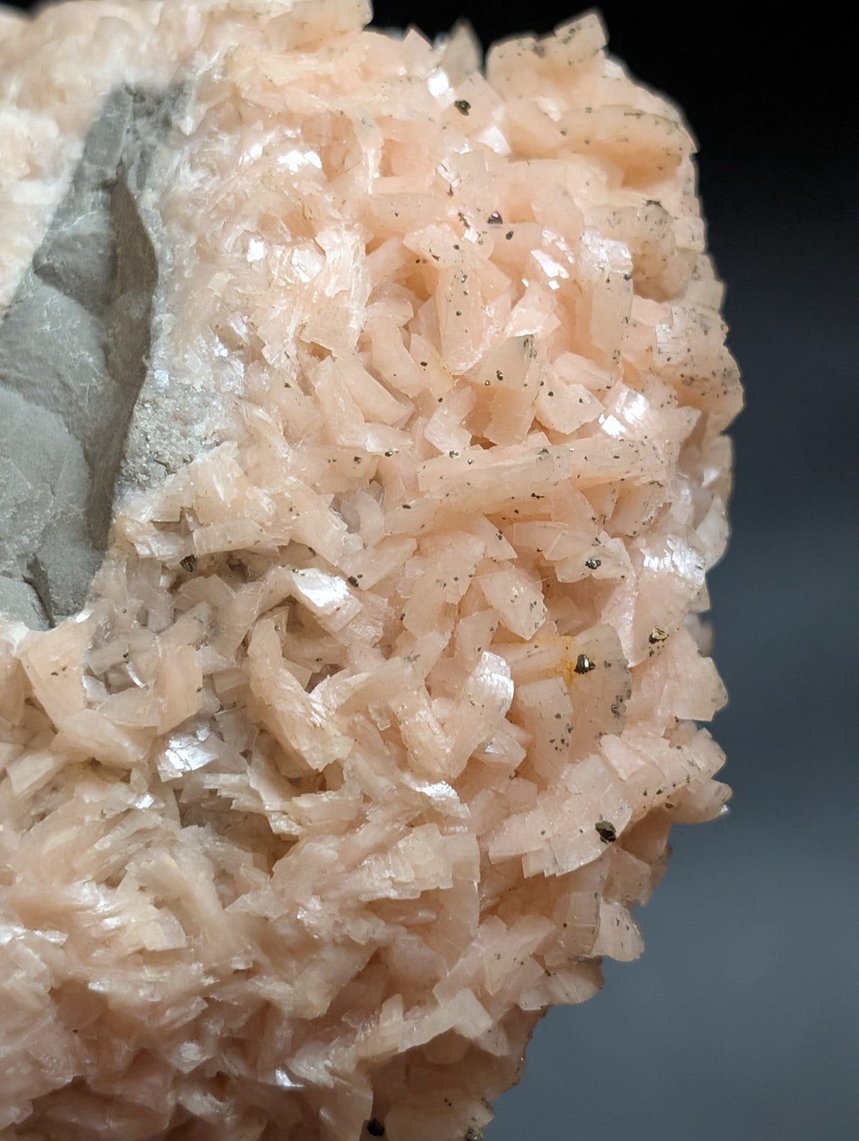 A cluster of translucent pink crystals with a rough, jagged surface and embedded dark specks.