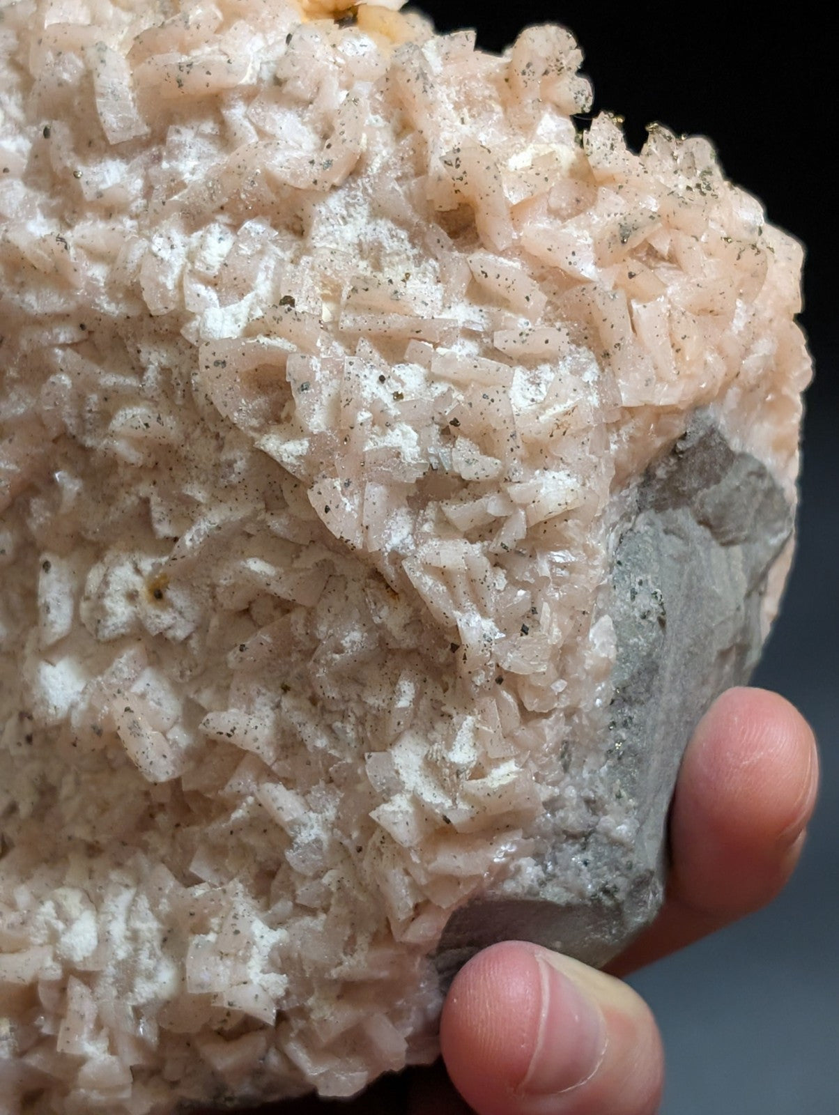 A pink, crystalline mineral specimen with a rough, textured surface and embedded dark specks.