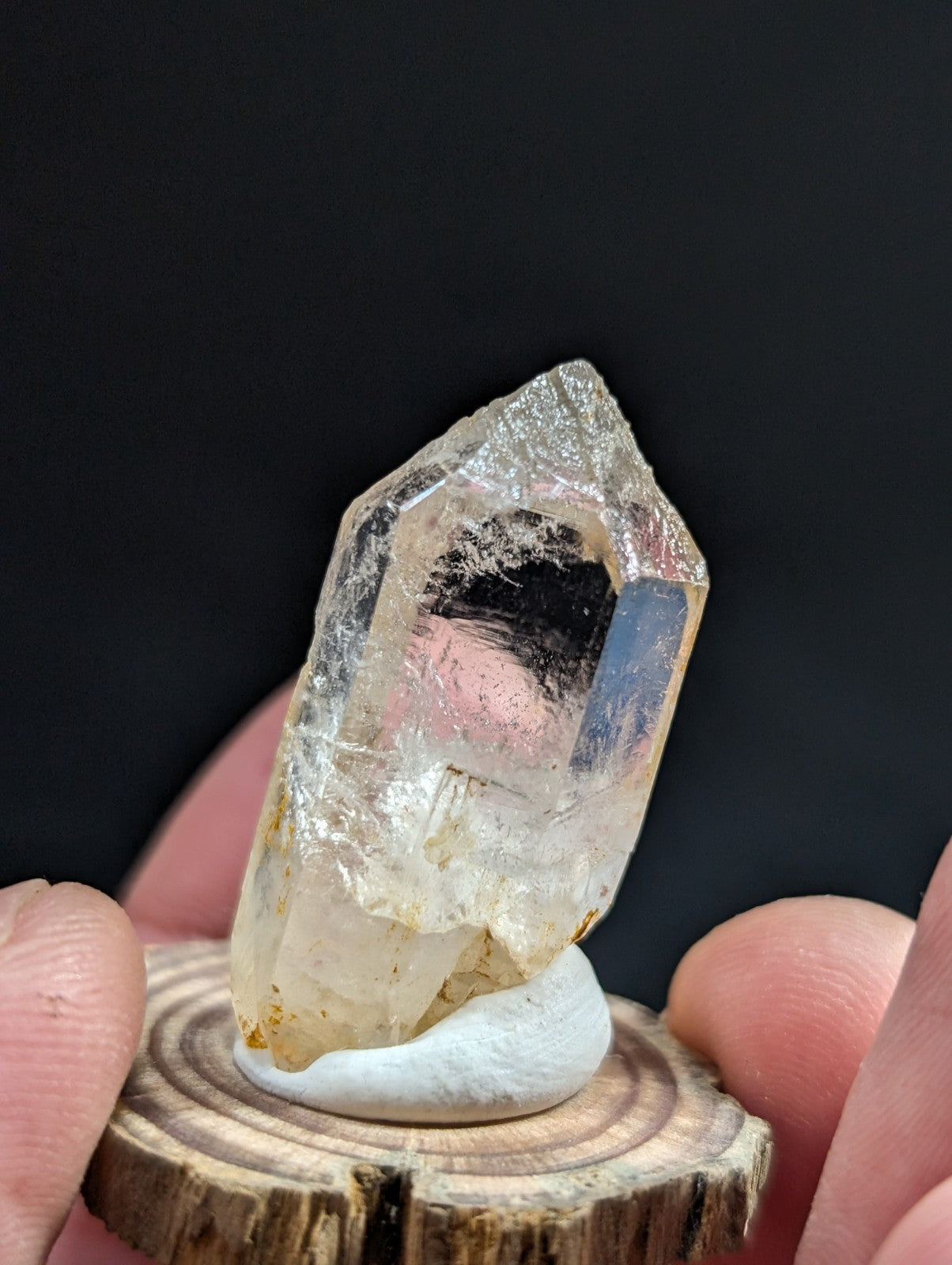 A translucent, pale yellow quartz crystal with a pointed tip and natural inclusions is displayed on a small wooden stand.