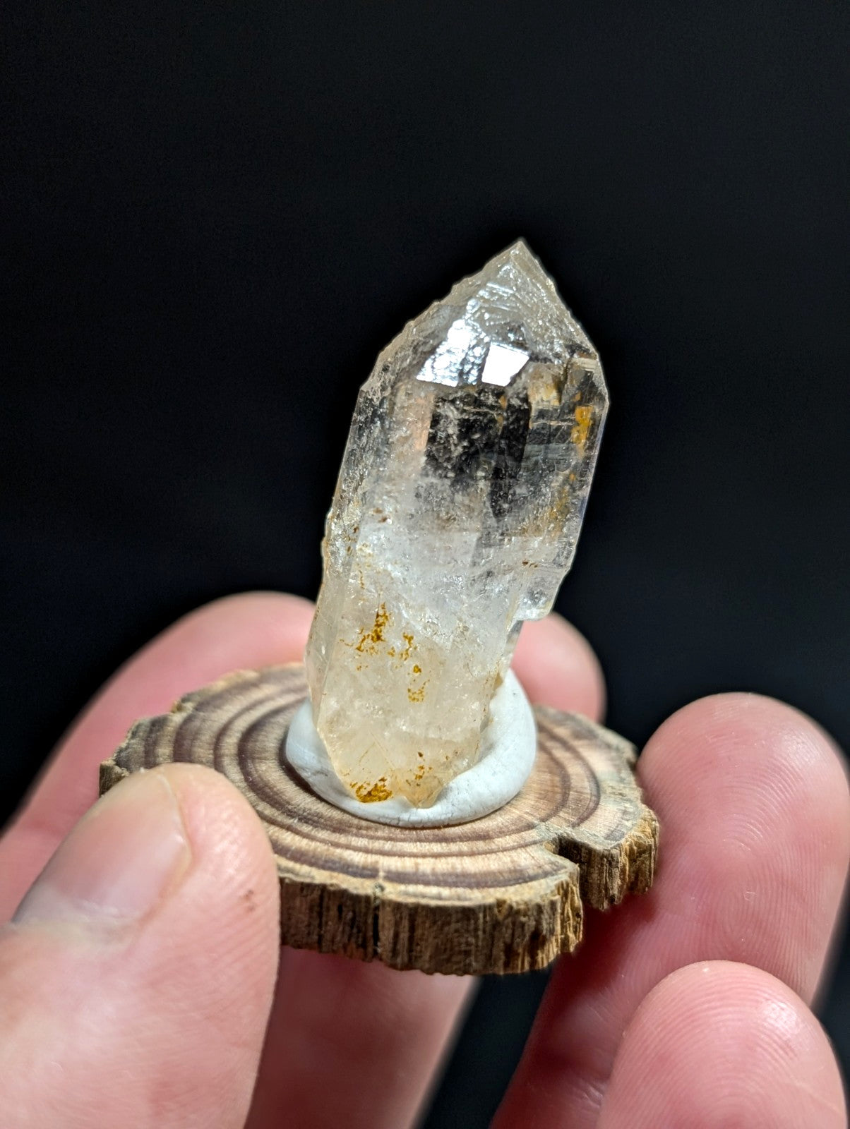 A translucent, faceted quartz crystal with golden inclusions stands upright on a circular wooden slice base.
