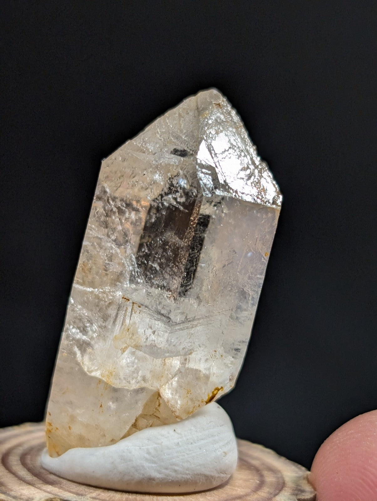 A translucent, clear quartz crystal with natural inclusions and a pointed tip, displayed on a white ceramic stand.