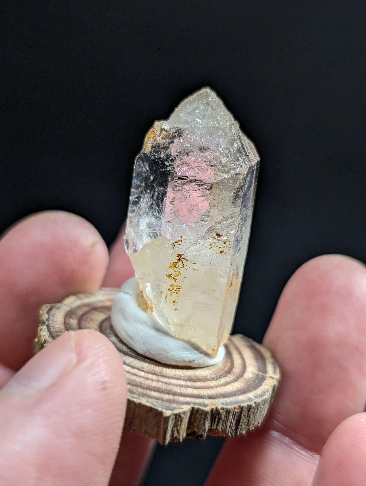 A translucent quartz crystal with pink and golden inclusions, displayed on a rustic wooden slice.