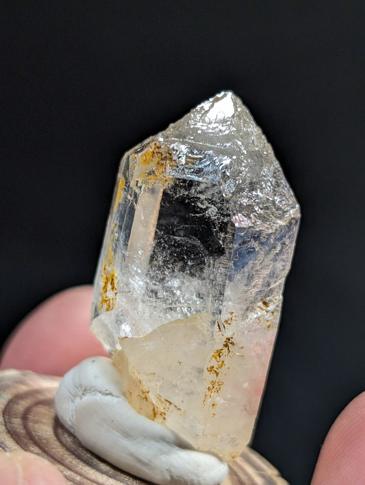 A translucent quartz crystal with golden inclusions, held gently by fingers against a dark background.