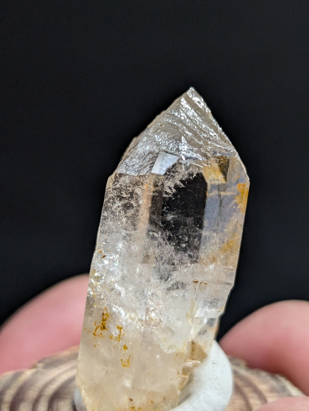 A translucent, clear quartz crystal with subtle golden and dark inclusions, held upright on a white display stand.