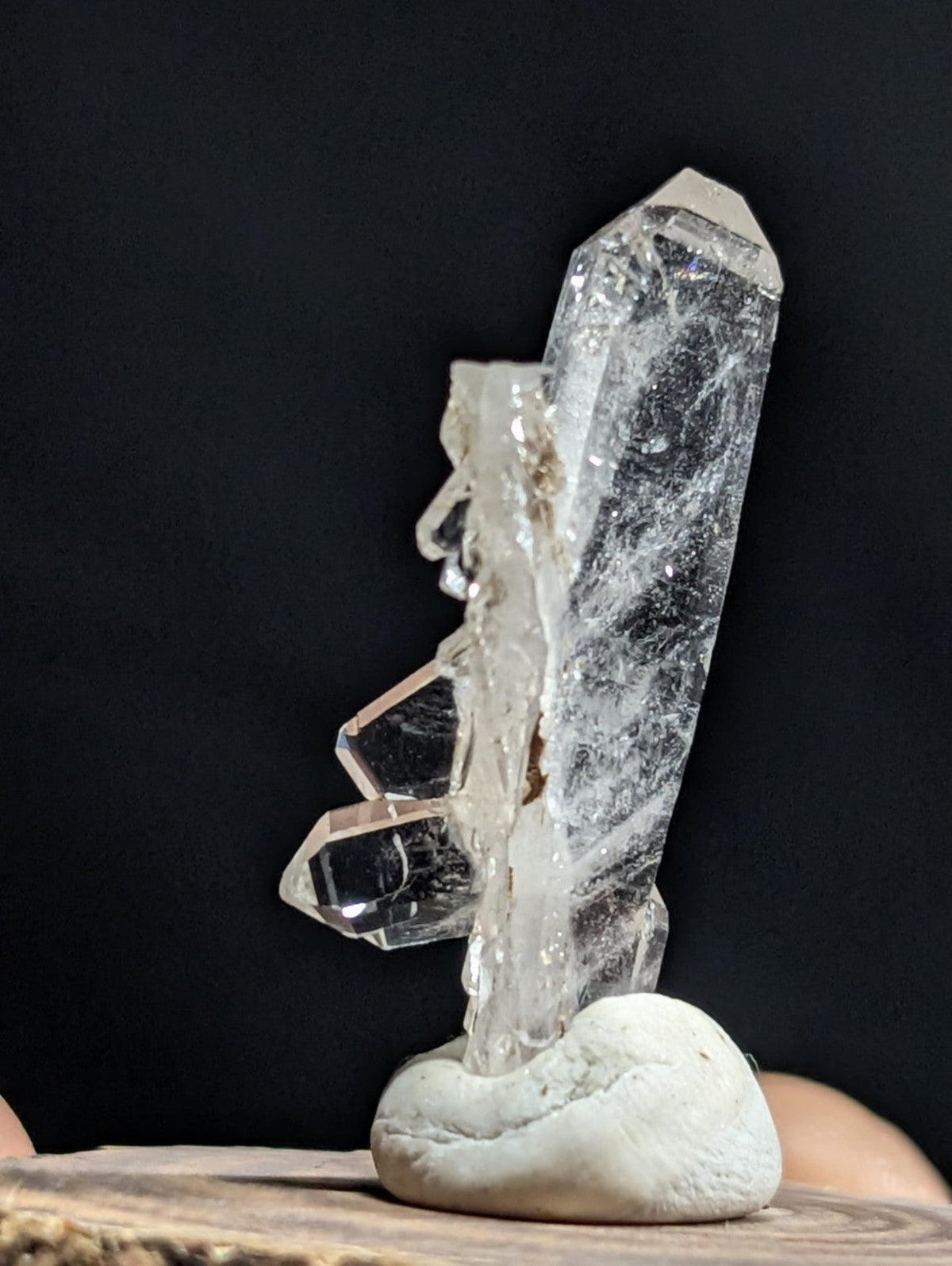 A clear quartz crystal cluster with sharp, faceted points and a translucent body rests on a smooth white stone base.