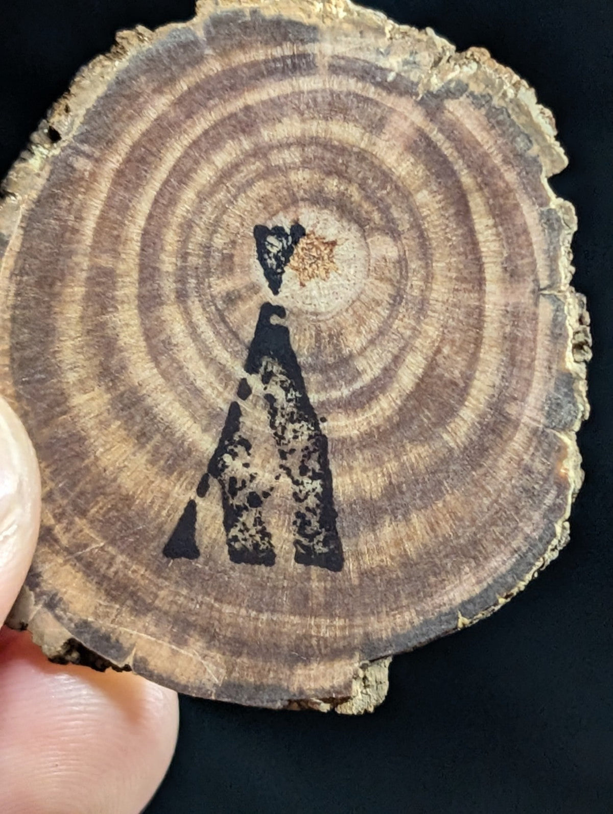 A rustic, circular wood slice with natural grain rings and a hand-painted black silhouette of a figure holding a star.