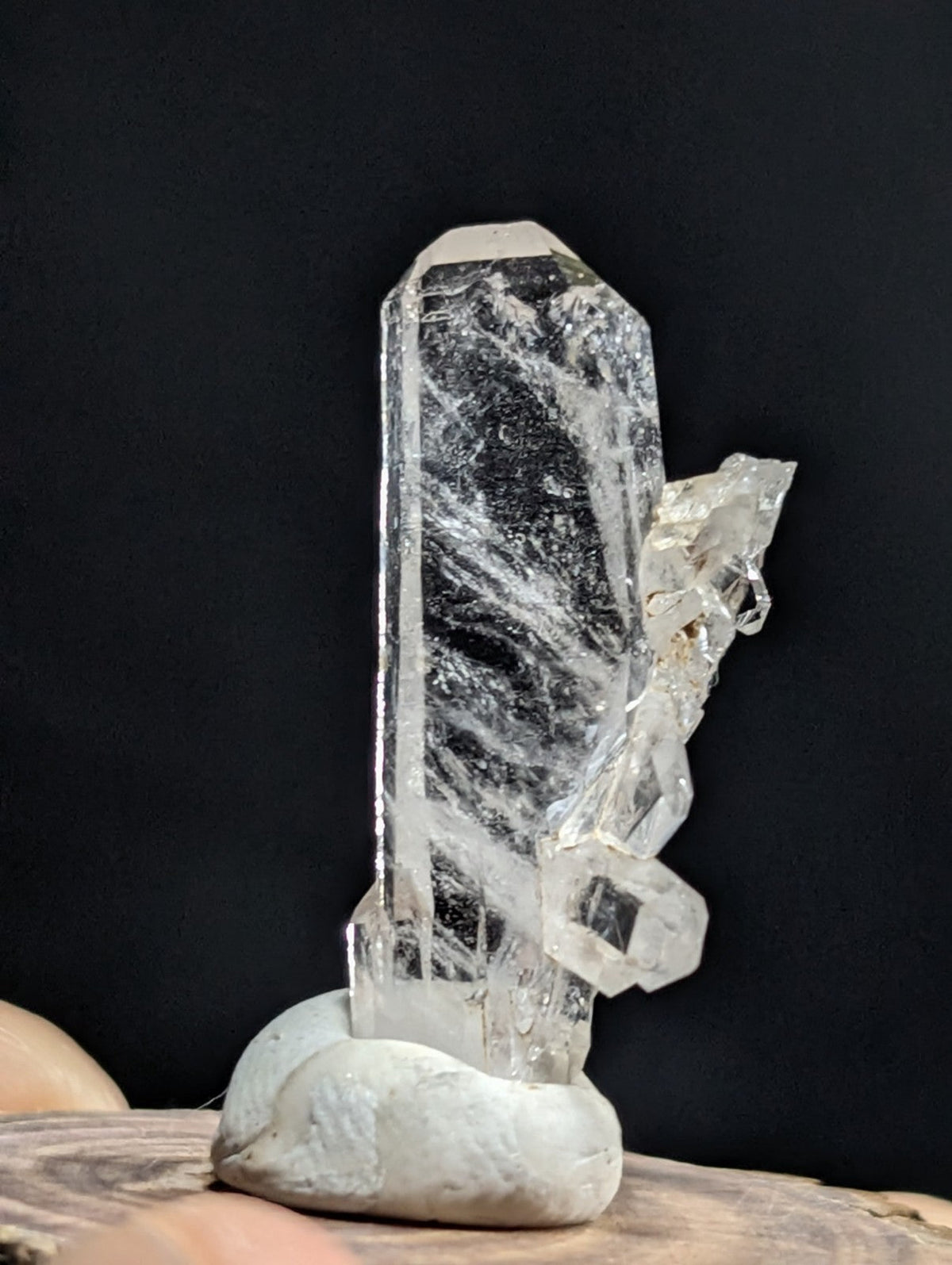 A clear quartz crystal with a tall, faceted main column and branching crystalline formations, mounted on a smooth gray stone base.