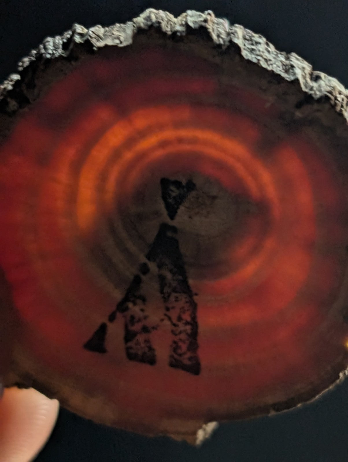 A polished red-orange agate slice with concentric rings and a dark, stylized letter ’a’ etched into its surface.