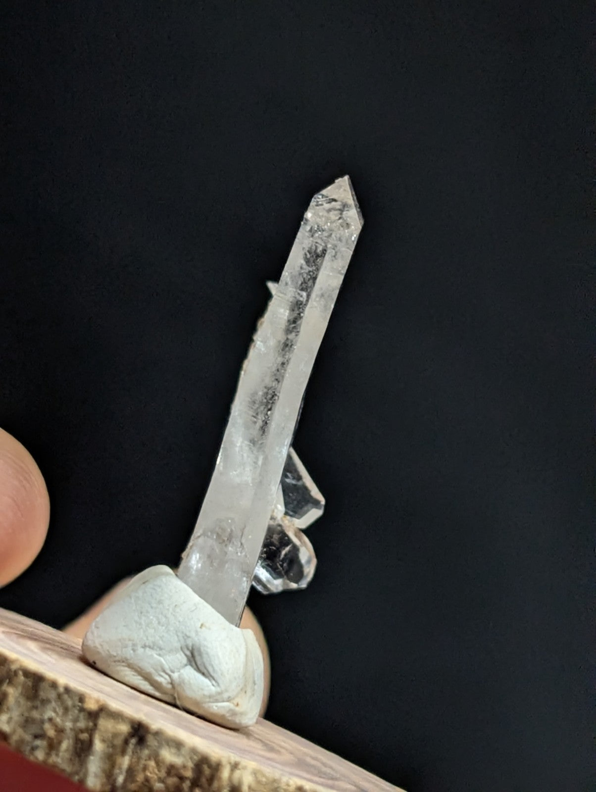 A clear quartz crystal with a pointed tip and visible internal inclusions, mounted on a light-colored stone base.
