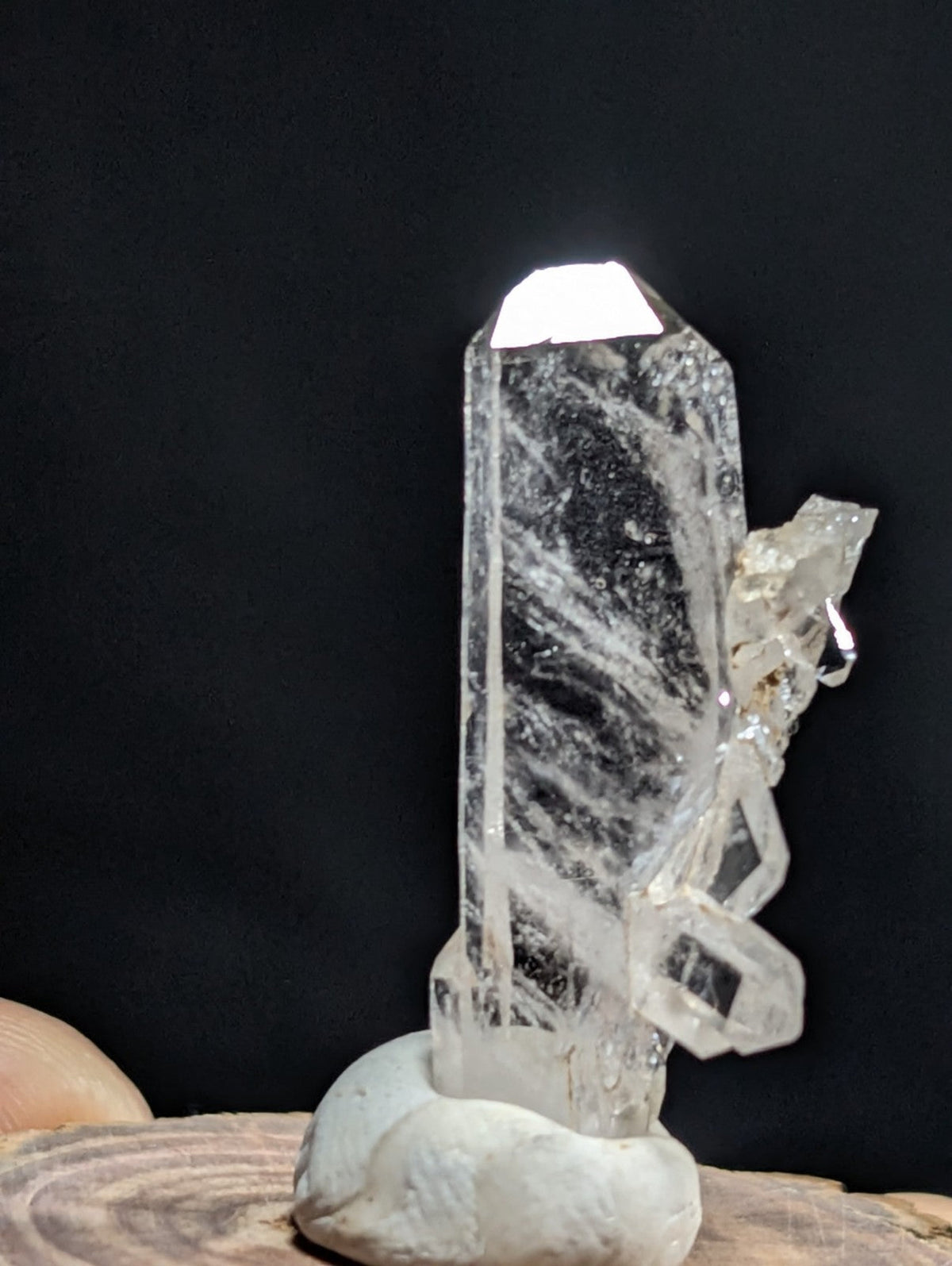 A clear quartz crystal with a tall, faceted column and intricate internal striations, mounted on a smooth white stone base.