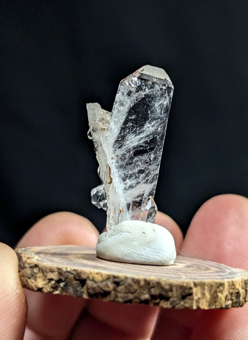 A clear quartz crystal cluster with a tall, faceted central point and smaller branching crystals, mounted on a smooth white stone base.