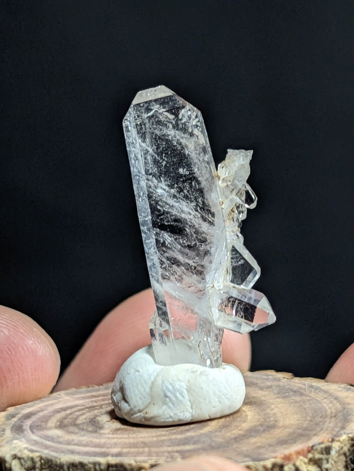 A clear quartz crystal cluster with a tall, faceted main point and smaller branching crystals, mounted on a smooth white base.