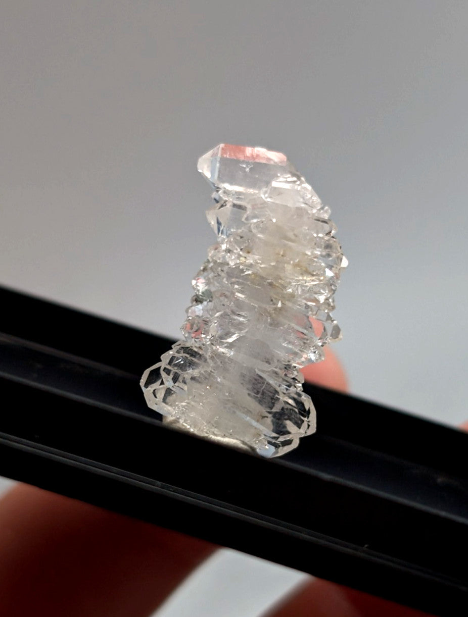 A translucent clear quartz crystal cluster with jagged facets and pinkish hue mounted in a photo case from Saline County Arkansas