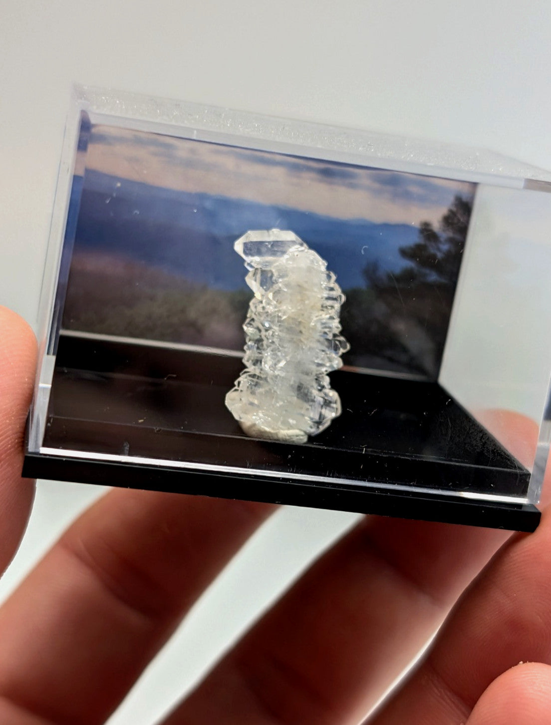 A clear, faceted quartz crystal specimen displayed in a transparent acrylic display case with a black base.