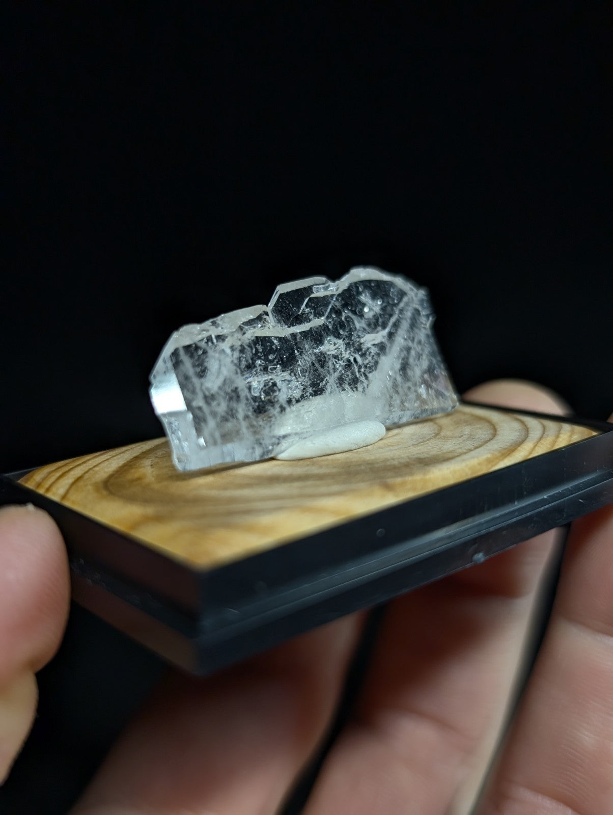 A translucent, clear quartz crystal with visible internal inclusions and a rough, faceted surface rests on a wooden display base.