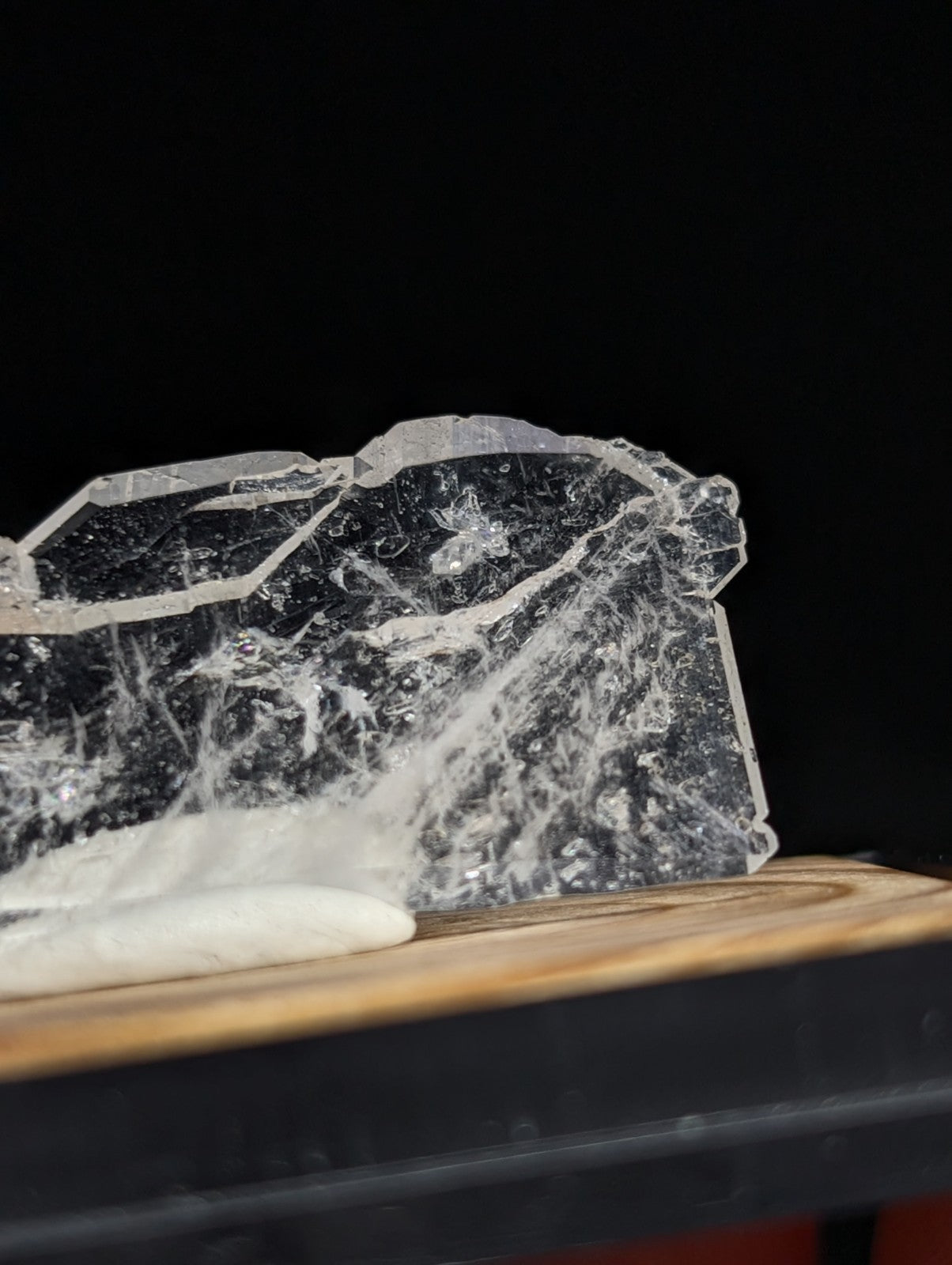 A translucent, jagged piece of crystal with internal web-like inclusions rests on a wooden surface.