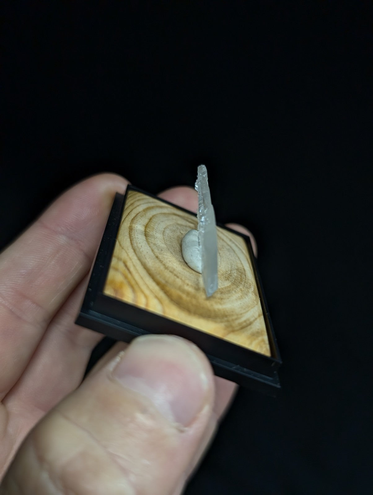 A translucent, crystalline mineral specimen mounted on a square wooden base with black framing.