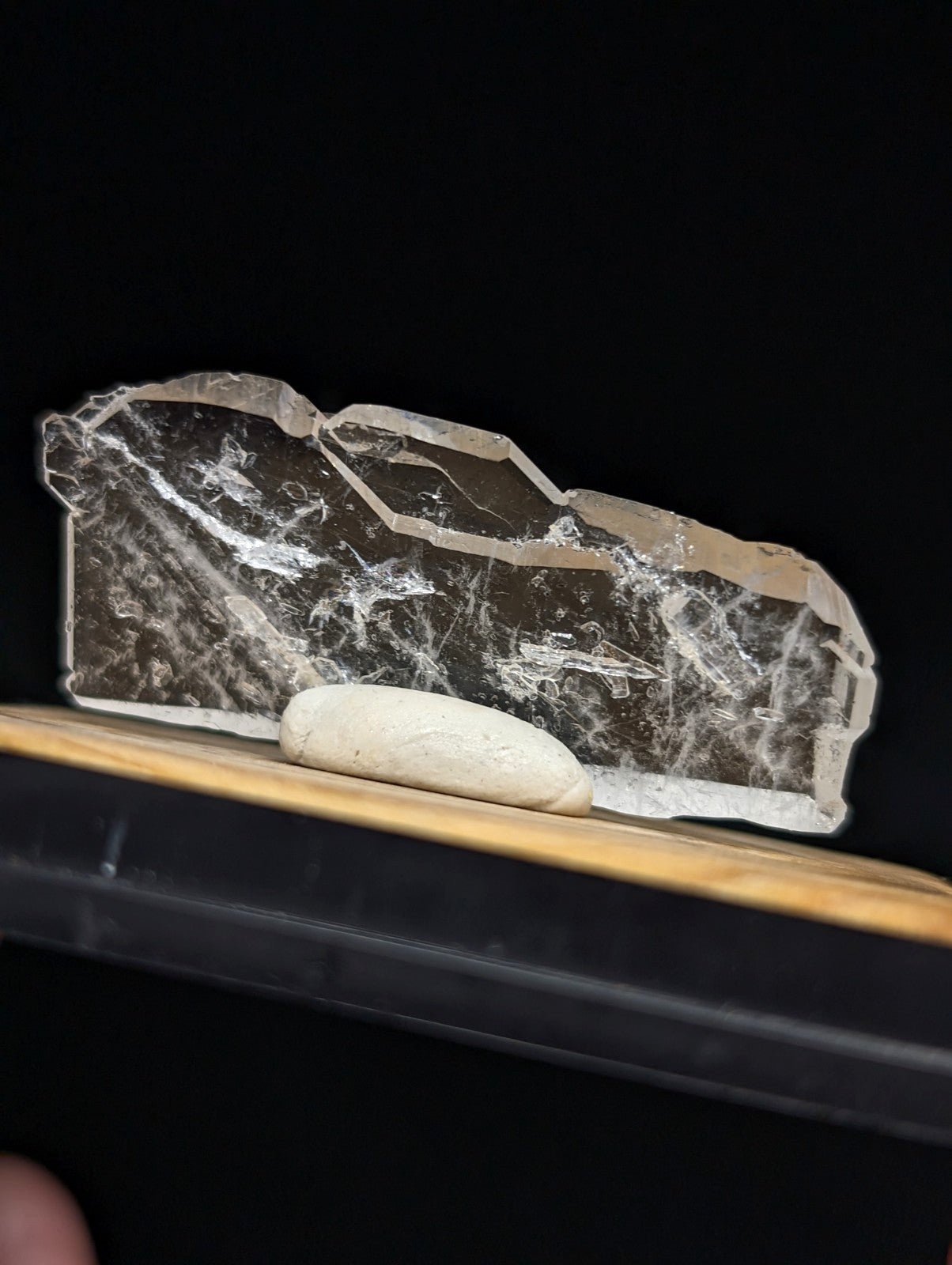 A translucent, irregularly shaped crystal with a dark interior and white veining rests on a wooden surface.