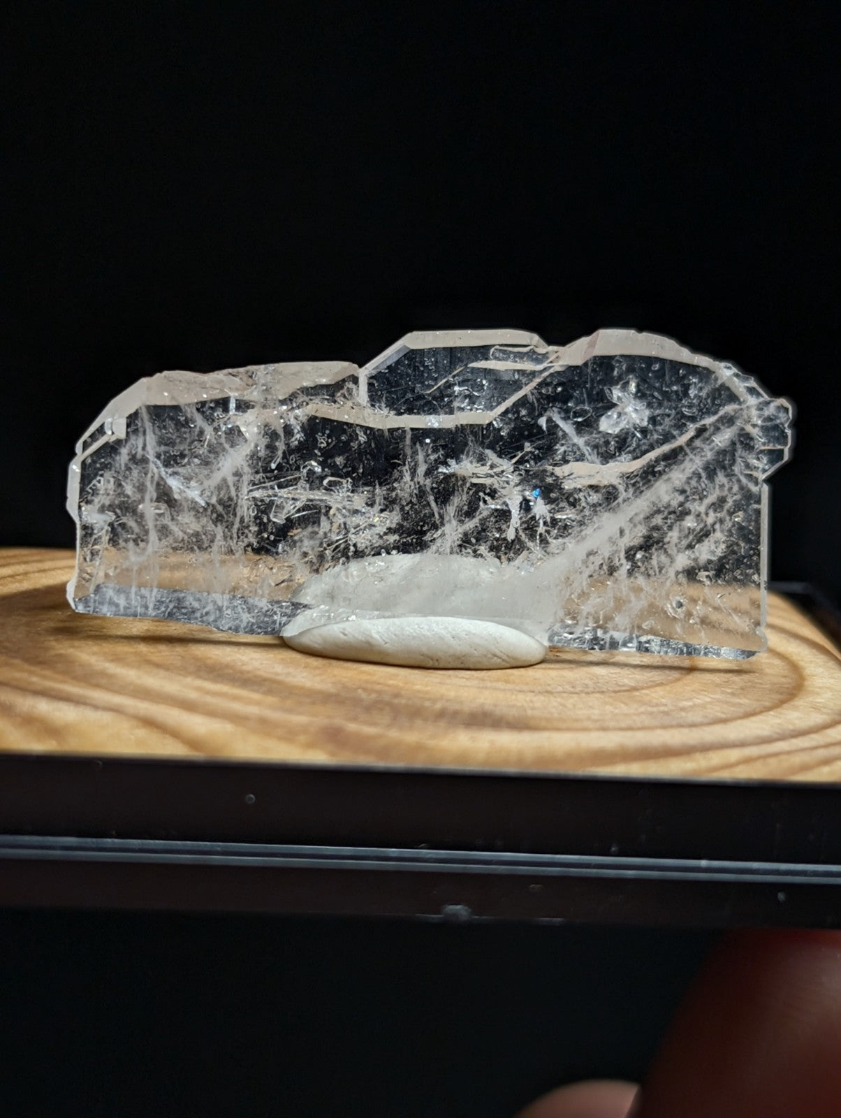 A translucent, clear crystal with intricate internal veining and a smooth, slightly rounded base rests on a wooden surface.