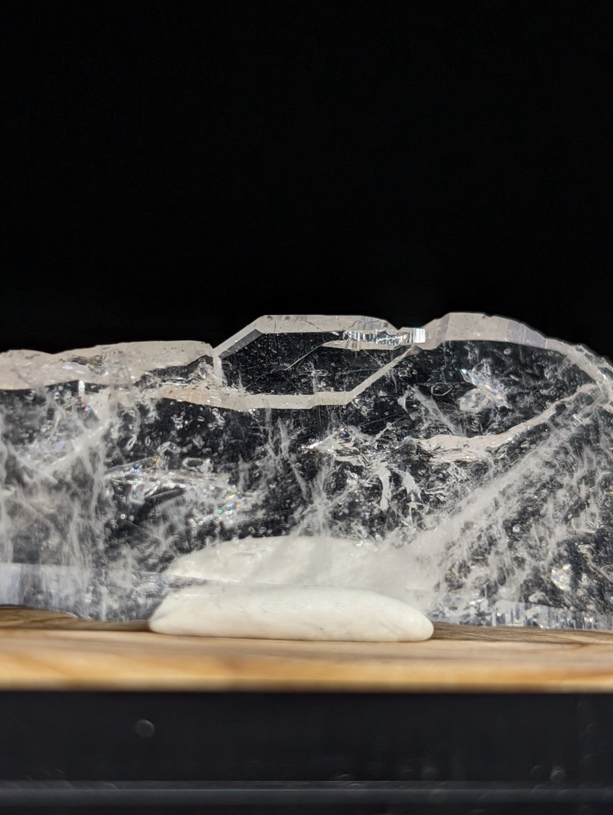 A translucent, jagged piece of ice with a crystalline structure and embedded air bubbles rests on a wooden surface.