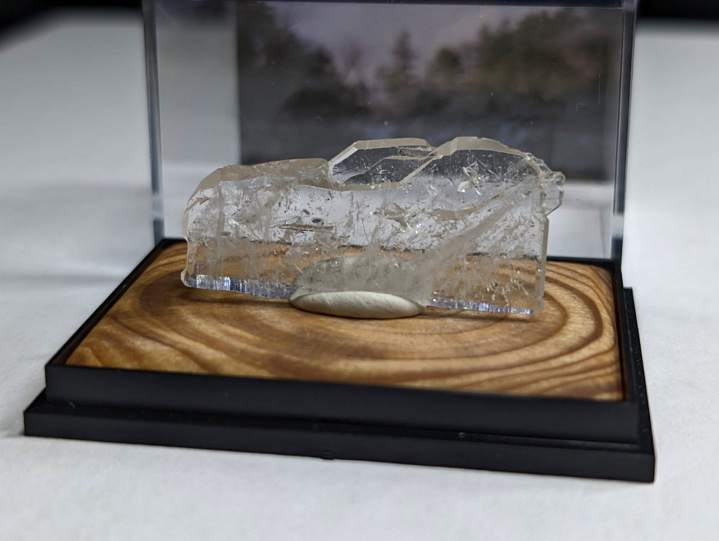 A clear, faceted quartz crystal specimen displayed in a transparent acrylic case on a wooden base.