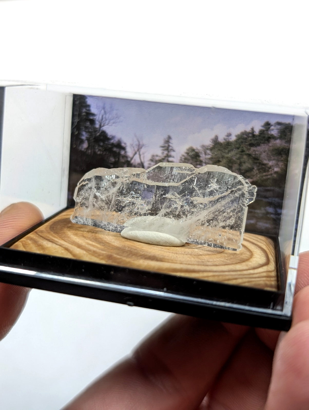 Clear, translucent crystal fragment with natural internal fractures and a smooth white stone base.