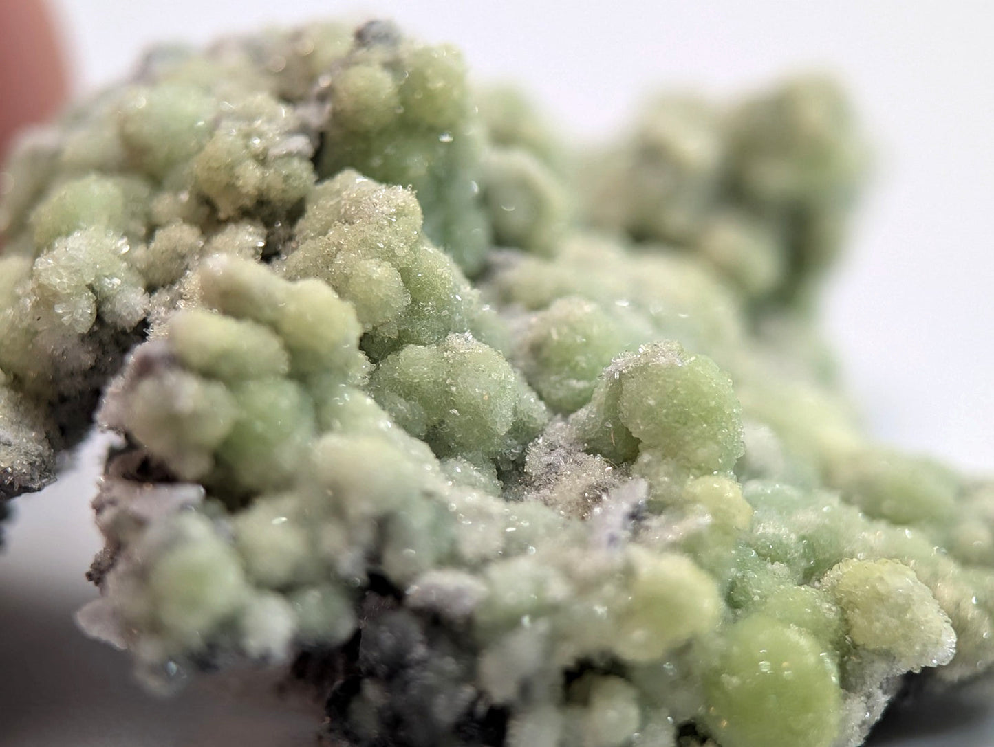 A cluster of pale green, crystalline minerals with a textured, bumpy surface and some translucent facets.