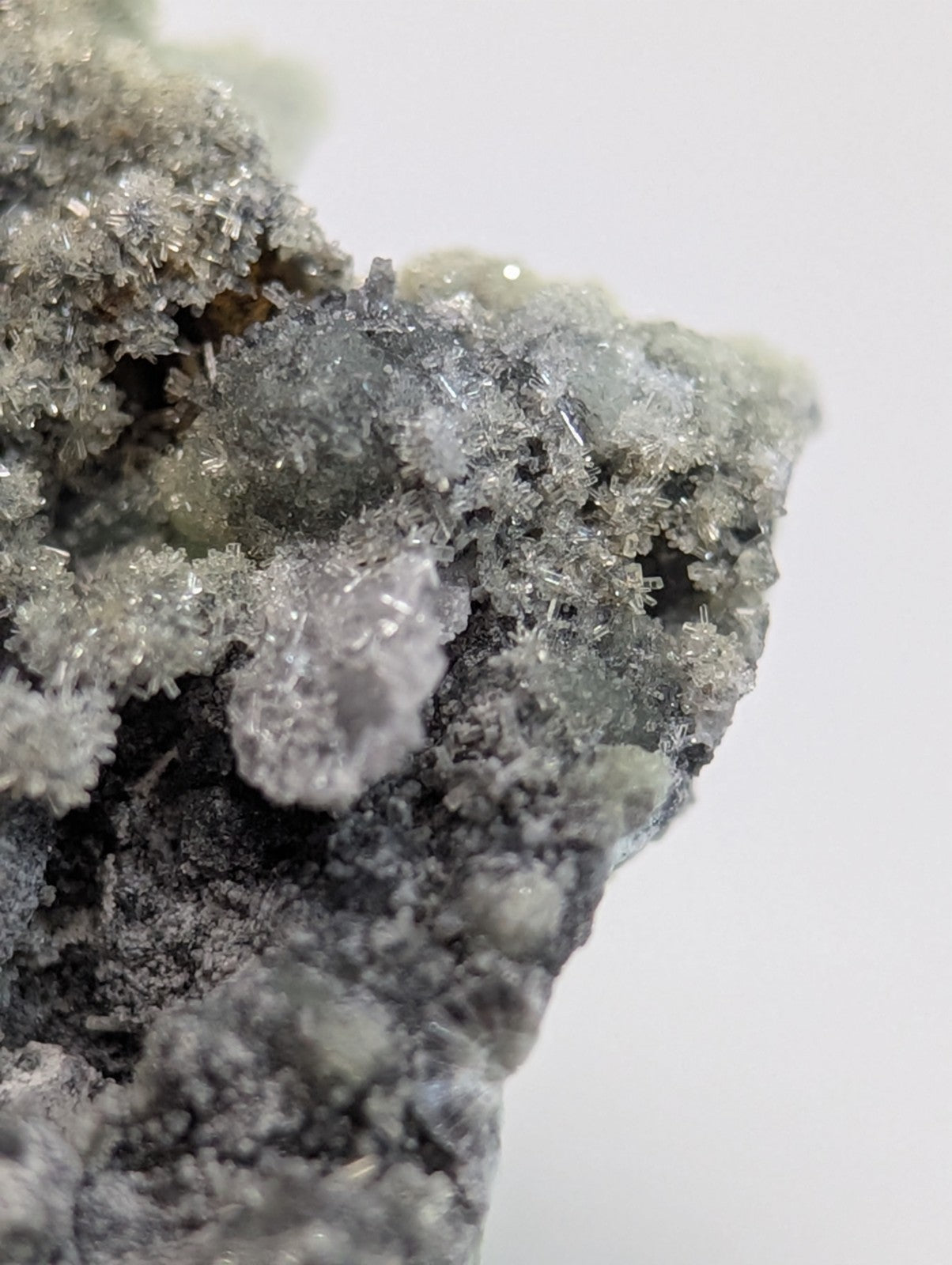 A grayish mineral specimen featuring a dense cluster of translucent, crystalline formations with sharp edges and subtle iridescence.