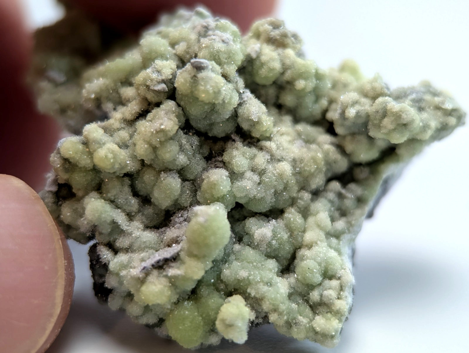 A cluster of pale green, crystalline minerals with a rough, textured surface.
