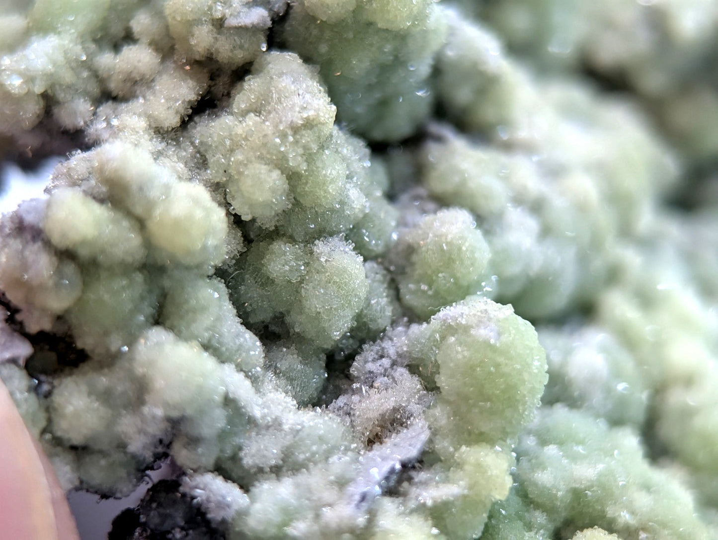 A cluster of pale green, crystalline mineral formations with a textured, sugary surface.