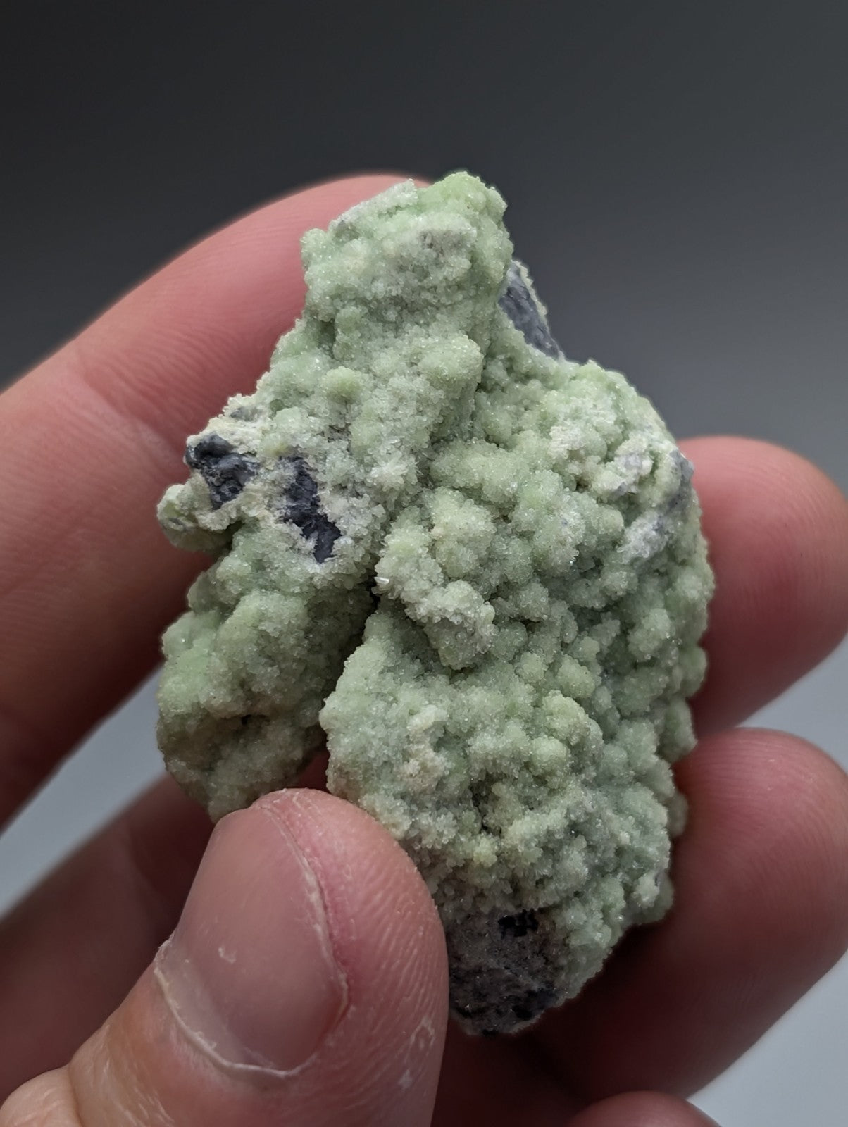 A pale green textured A+ fluorwavellite mineral with dark inclusions intermixed with SiO2 from Mauldin Mountain Arkansas held gently