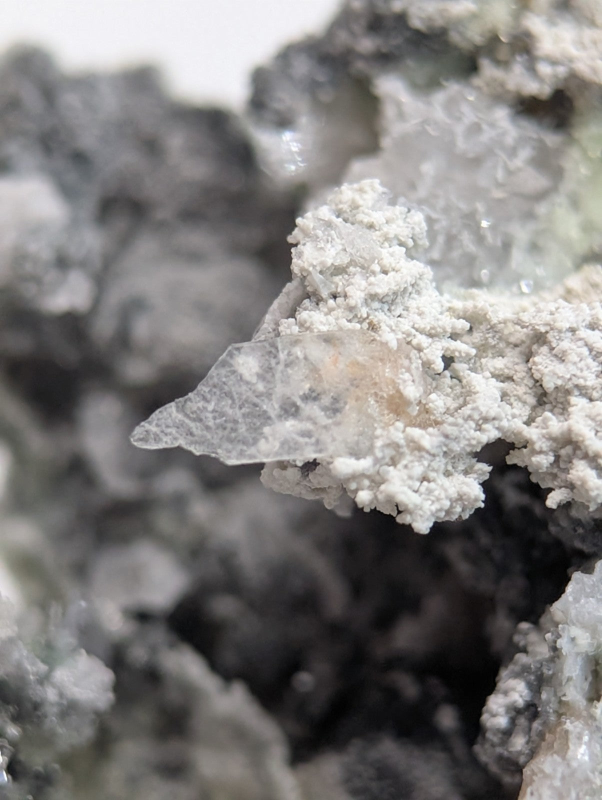 A translucent, crystalline mineral formation with a pointed tip and embedded white powdery material.